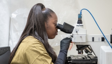 Daisy Ademoye looking into a powerful microscope in the Mind and Brain lab