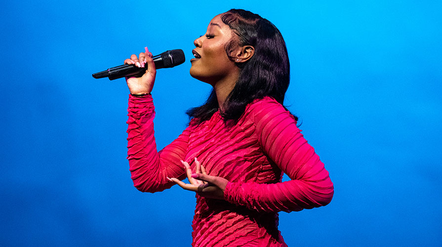 An Occidental College student sings into a mic on Apollo night, wearing a hot pink dress