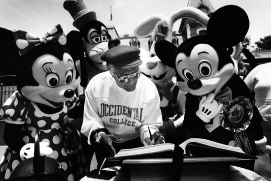 Desmond Tutu signs the Disneyland guestbook Minnie and Mickey Mouse look on.