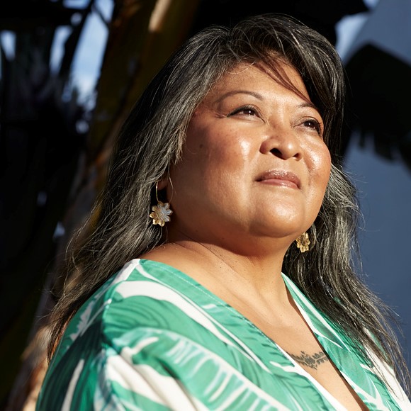 Portrait of a woman with long hair looking into the distance. She is wearing a green top. 