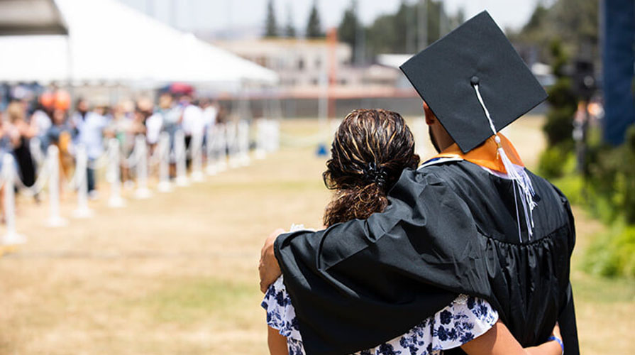 a student in college graduation dress hugs his mother