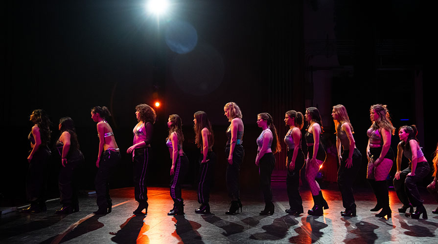 A line of Occidental College students on a shadowy stage during a Dance Pro dress rehearsal