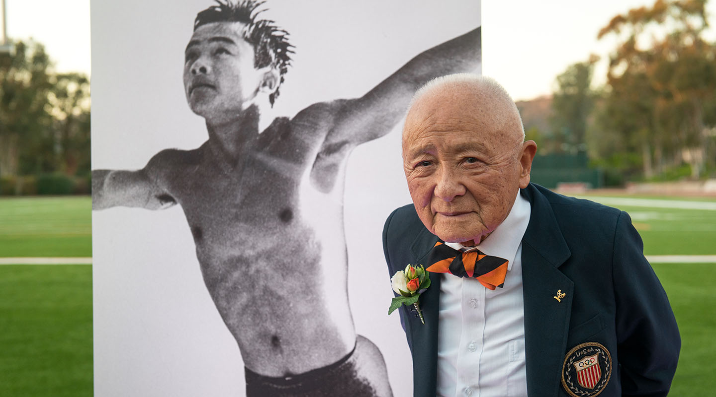 Sammy Lee Occidental College Olympian standing in front of a photo of him as a young man diving