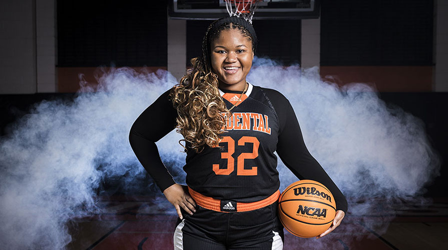 Alyanna McGrath portrait on a basketball court with a basketball and her Occidental College uniform