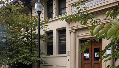 Swan Hall at Occidental College: a cream colored building with two wood doors with trees in front