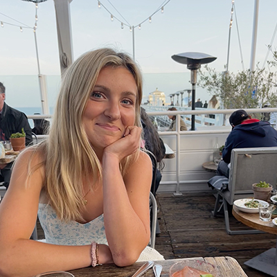 Grace is sitting at a table with the ocean in the background