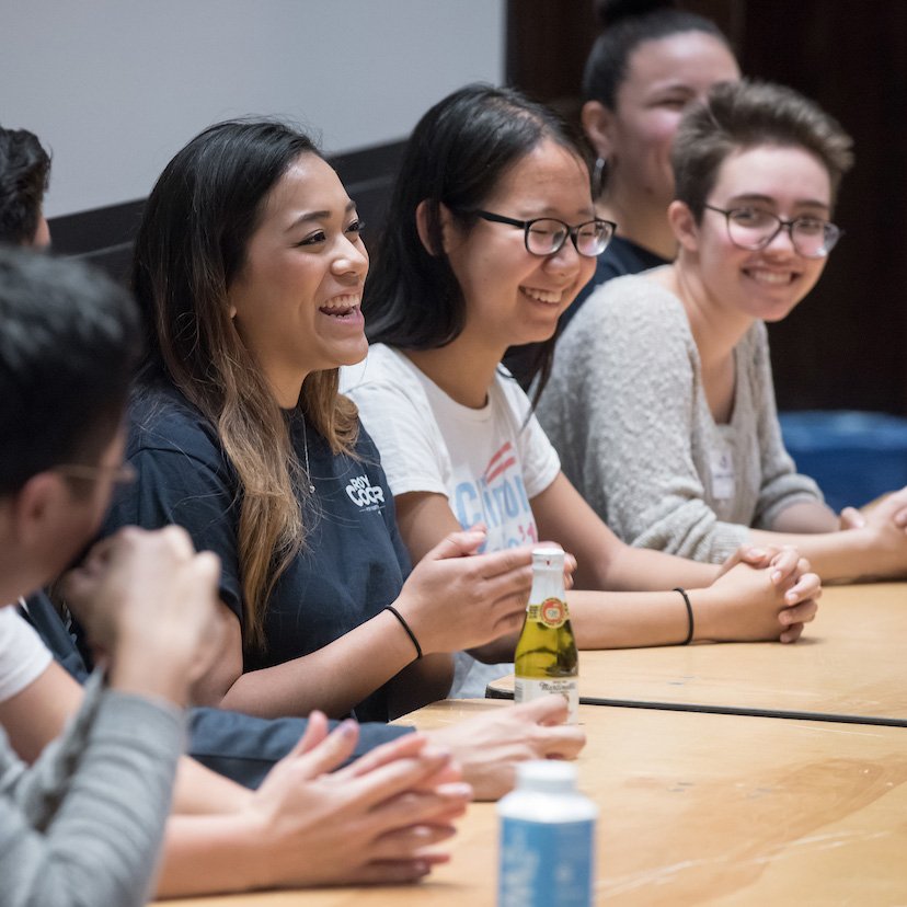 Students sitting in a row along a bench, smiling and talking 