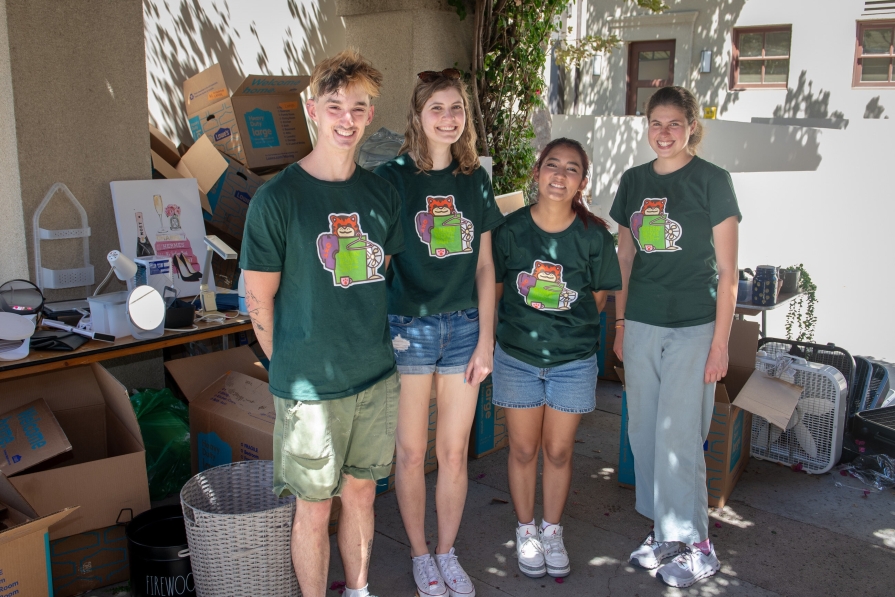 Green Move Out Volunteers wearing green tee shirts, a pile of used dorm goods is behind them