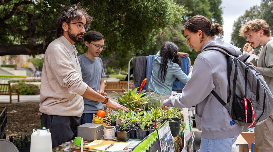Occidental students at an Earth Month table looking at small green plants