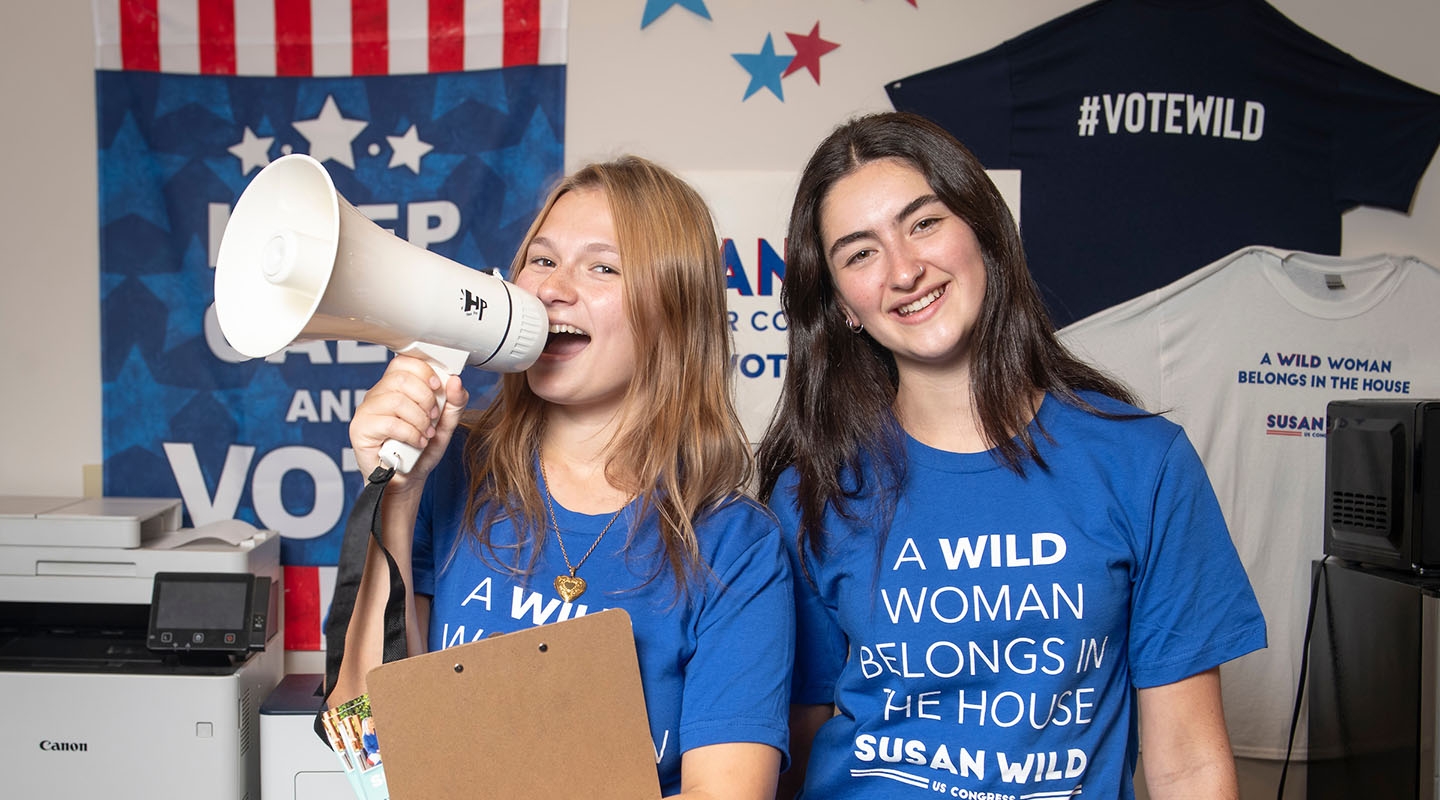 Two female Occidental students stand together with clipboards, a megaphone and blue campaign tshirts