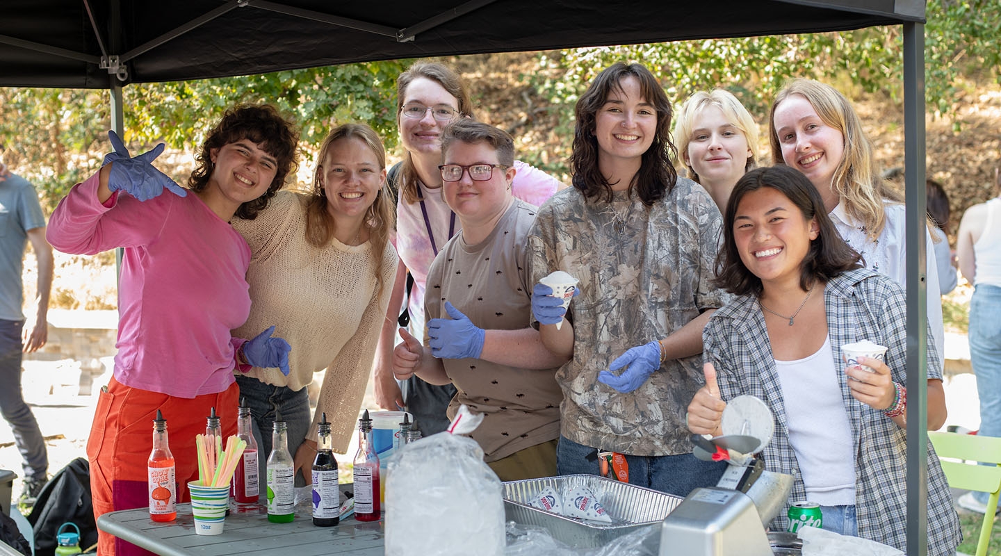 A happy group of Occidental College students posing together at a snow cone assembly table