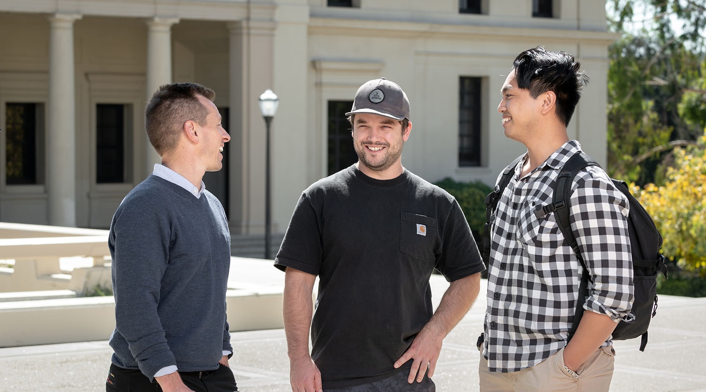 Three Occidental College veteran students stand together, talking and laughing