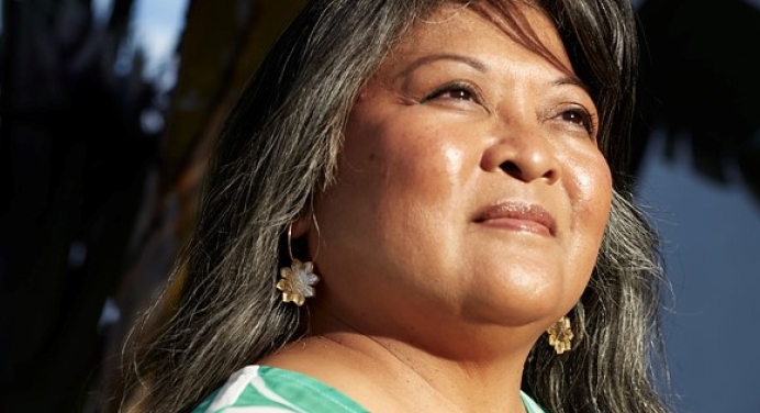 Portrait of a woman with long hair looking into the distance. She is wearing a green top. 