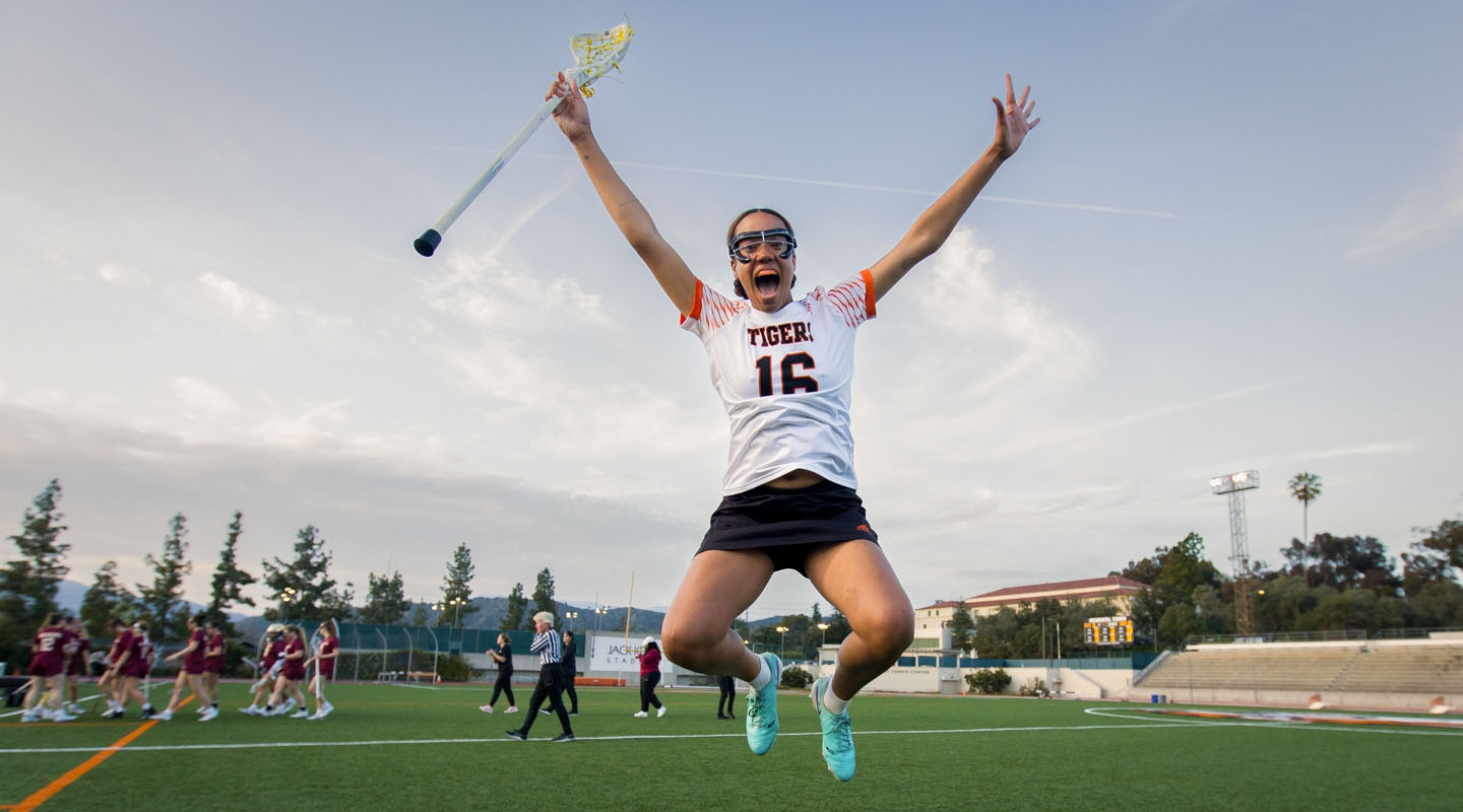 An Occidental College lacrosse player jumps into the air joyfully after a team victory