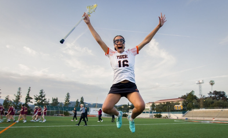 An Occidental College lacrosse player jumps into the air joyfully after a team victory