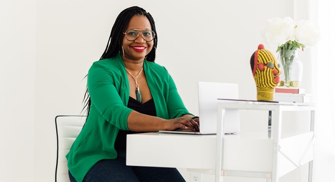 A smiling Deirdre Cooper Owens sitting at a desk with a green jacket