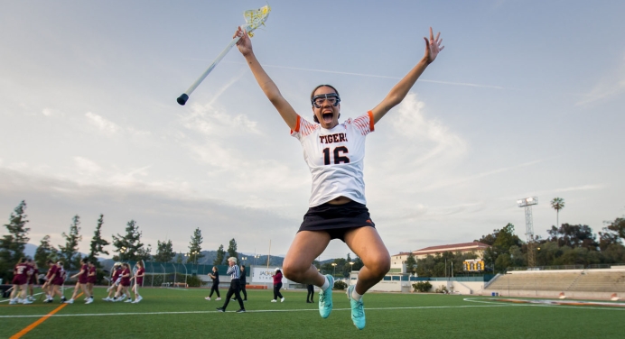 An Occidental College lacrosse player jumps into the air joyfully after a team victory