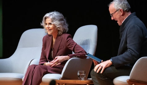 Jane Fonda sitting in a chair on an Occidental College stage in a maroon suit