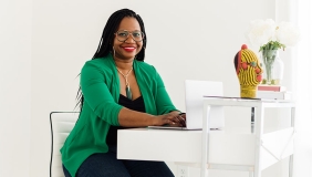 A smiling Deirdre Cooper Owens sitting at a desk with a green jacket