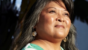 Portrait of a woman with long hair looking into the distance. She is wearing a green top. 