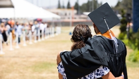 a student in college graduation dress hugs his mother