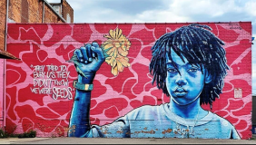 A mural depicting a black youth with fist raised, wrapped around a yellow flower. To the right of his hand, the text reads "They tried to bury us. They didn't know we were seeds."