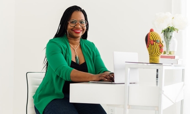 A smiling Deirdre Cooper Owens sitting at a desk with a green jacket