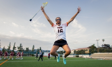 An Occidental College lacrosse player jumps into the air joyfully after a team victory