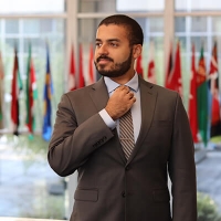 Jacob is wearing a suit and is standing in front of several flags