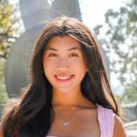 Lauren is wearing a pink shirt and is standing in front of a fountain