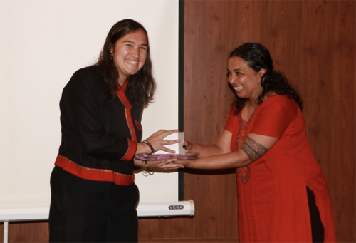 Leela, left, shakes the hand of a smiling woman in a red tunic