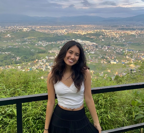 Reyan poses in front of an expansive view of green fields and blue mountains